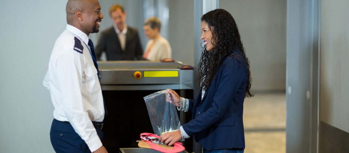 Smiling commuter interacting with airport security officer while collecting accessories from crate in airport